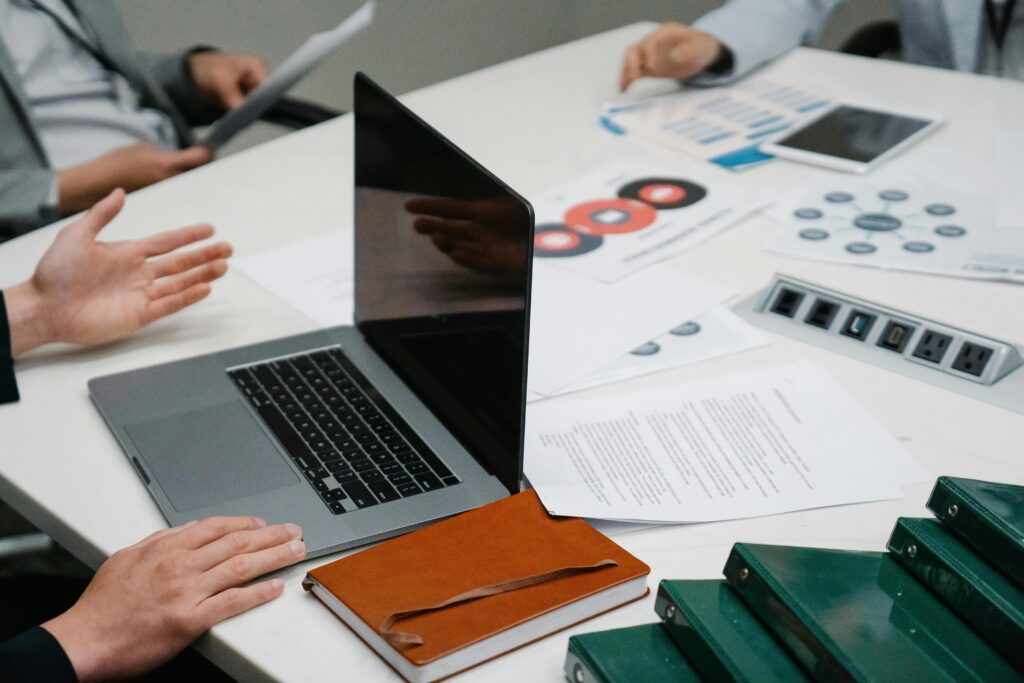pexels-photo-7964540-7964540 Close-up of a business meeting table with a laptop, documents, and discussion underway.